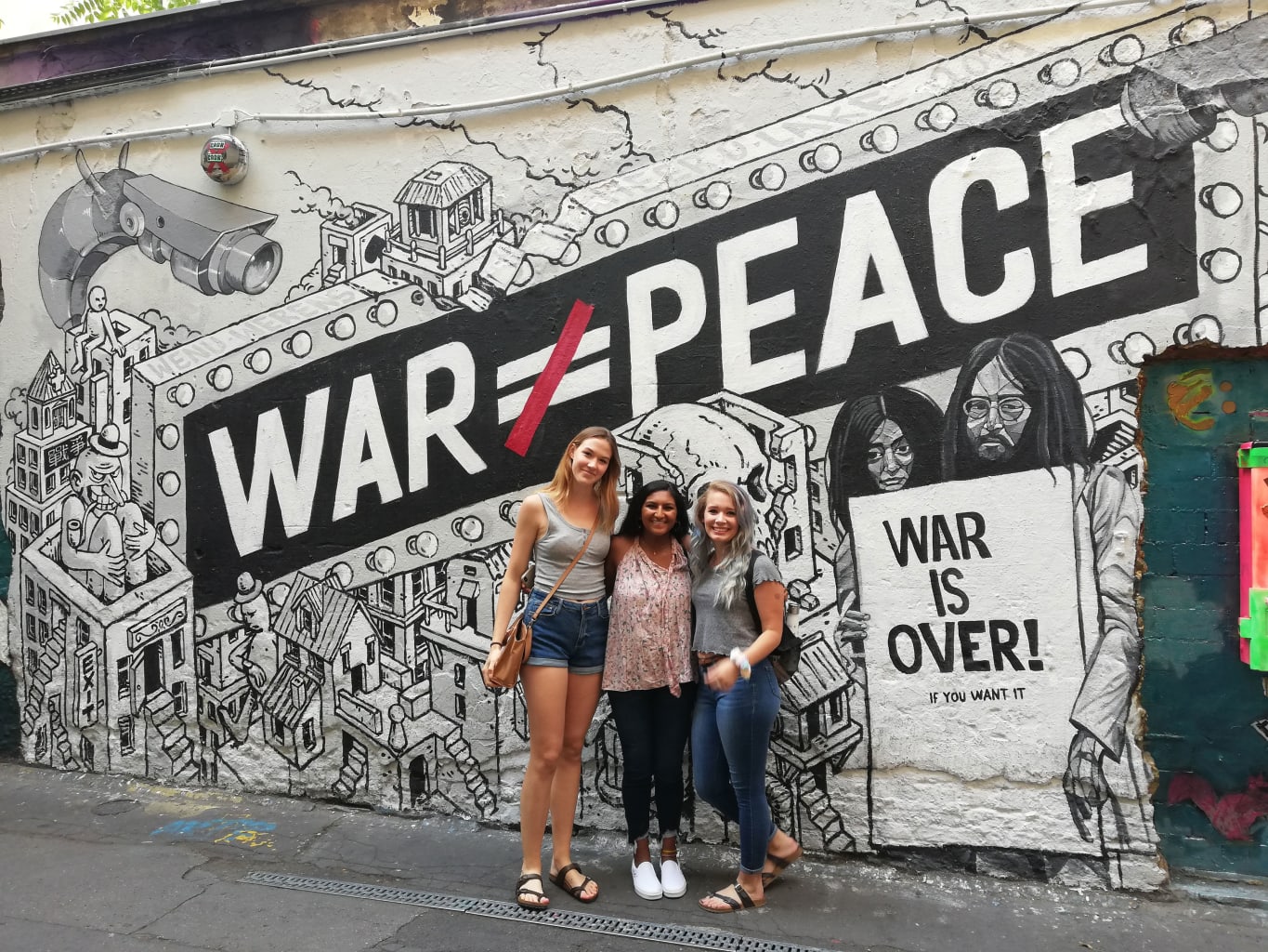 Three students in front of a mural.