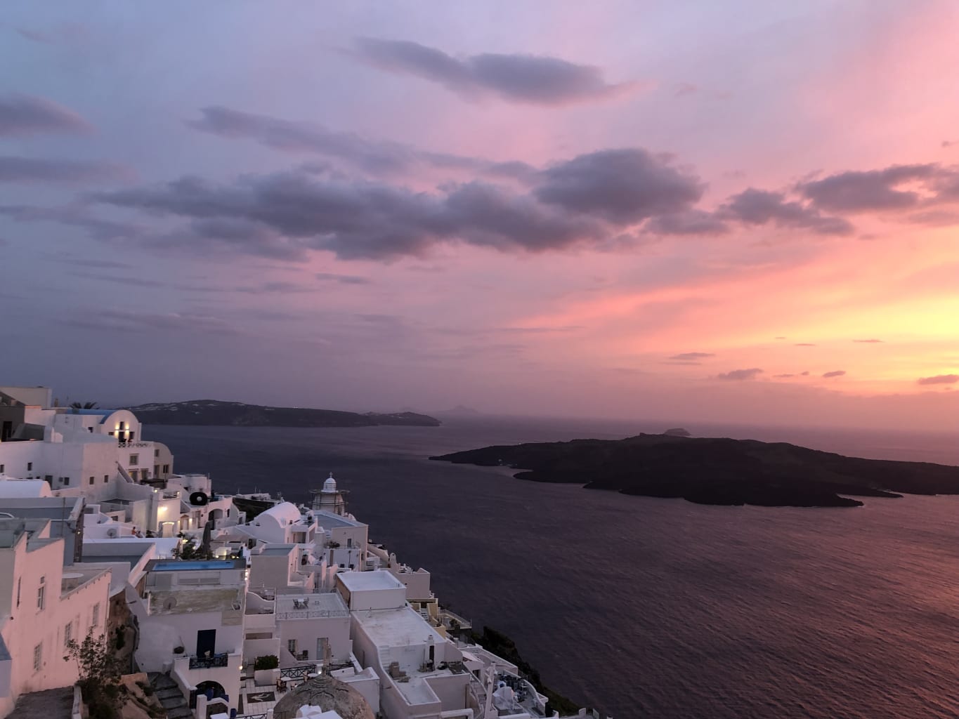 A view of a sunset over the ocean in front of a city in Greece.