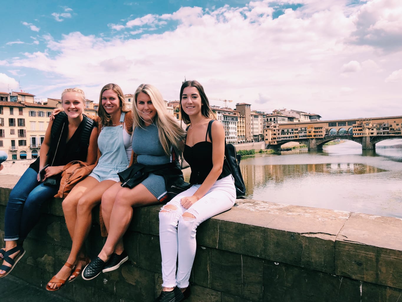 A group of students sitting on a bridge in Italy.