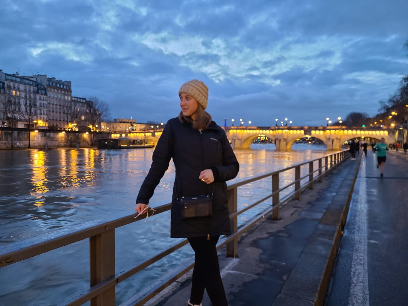 A student standing near a river in Paris during the evening.
