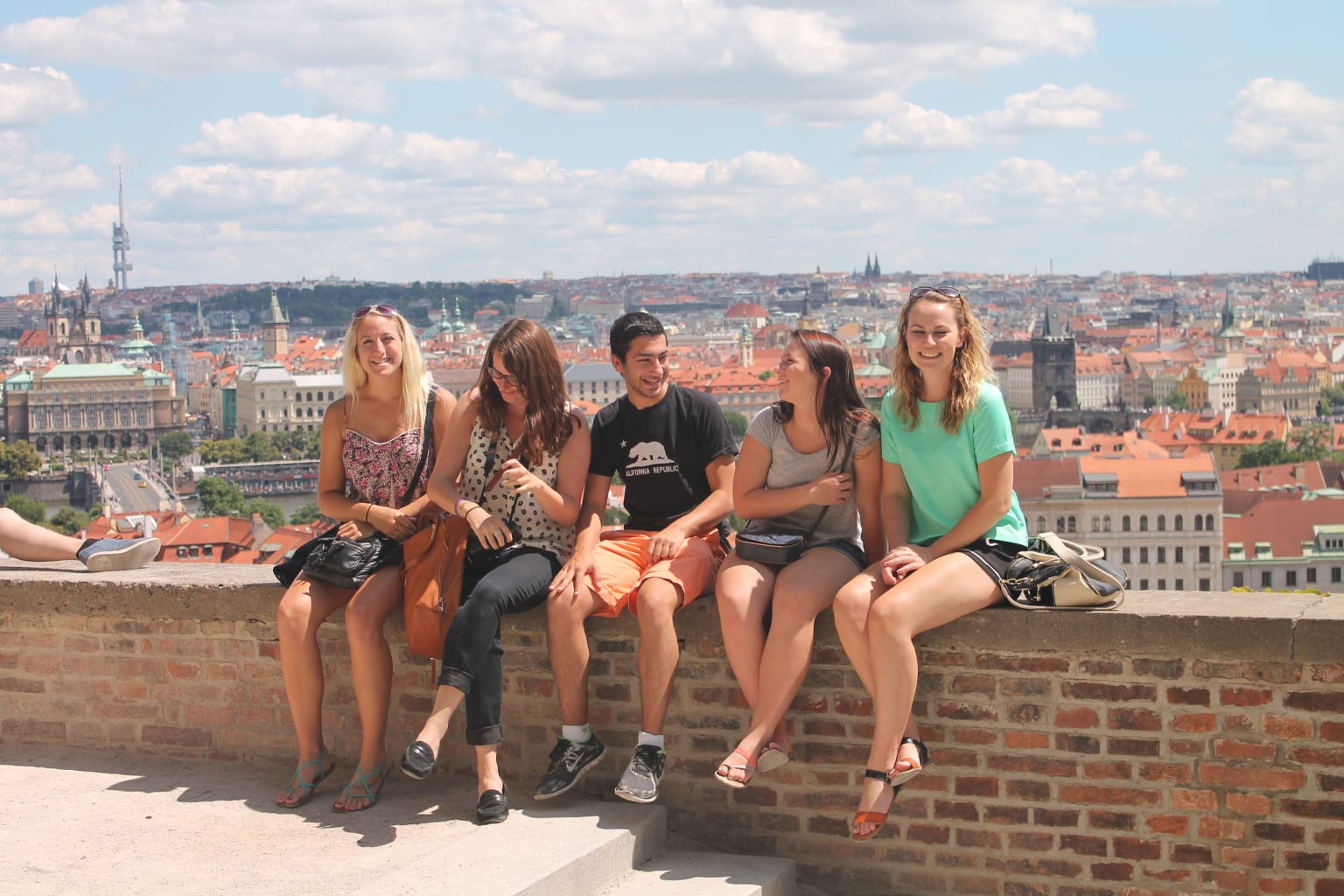 A group of students sitting on a ledge with a view of Prague in the background.