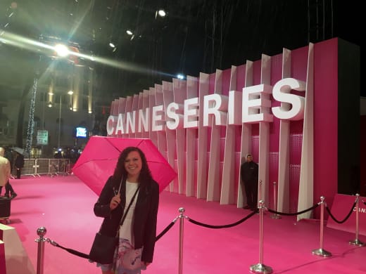 A student holding an umbrella in front of a sign that reads, "CANNESERIES" in Cannes, France.