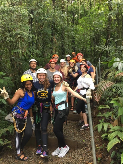 A group of students wearing helmets and harnesses in a forest.