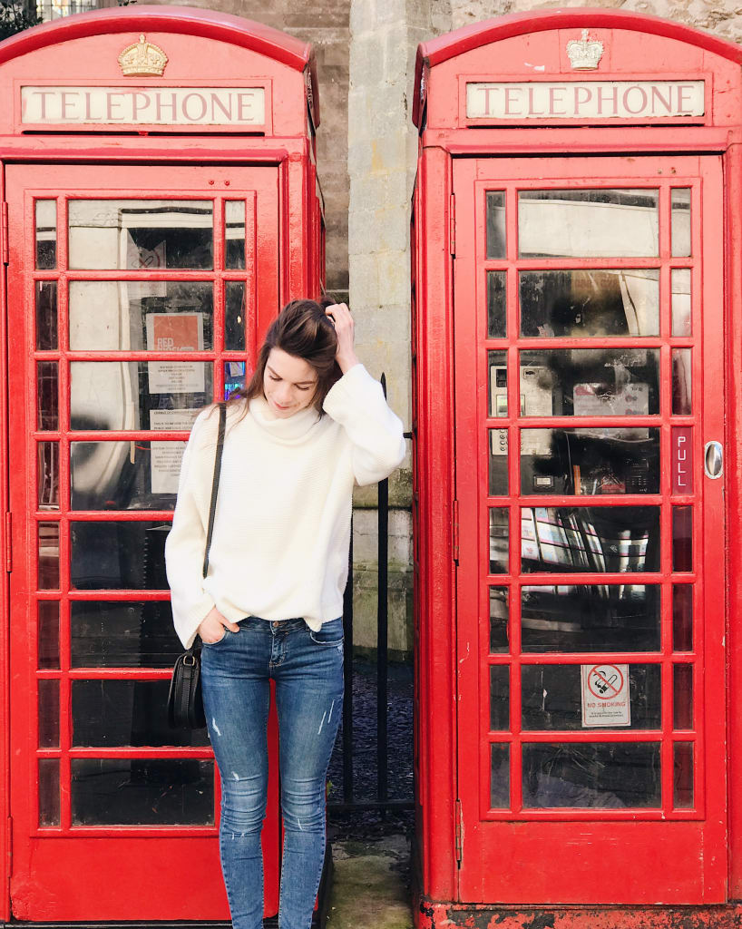 A woman in front of two red telephone booths in London, England.