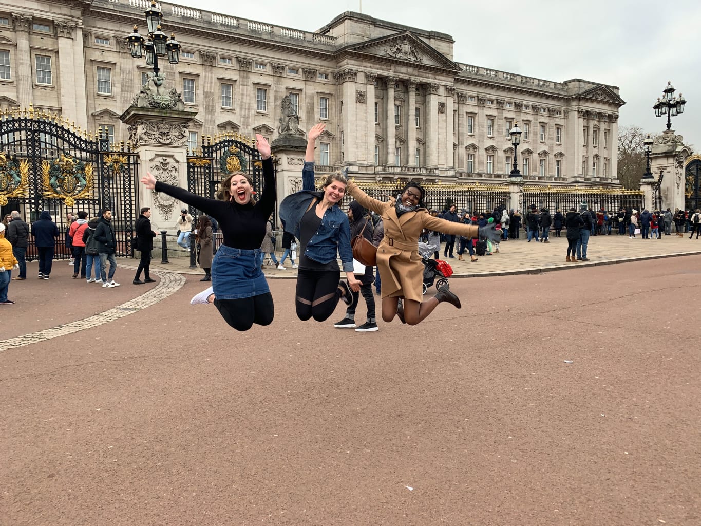 Three women jumping in the air in front of Buckingham Palace in London.