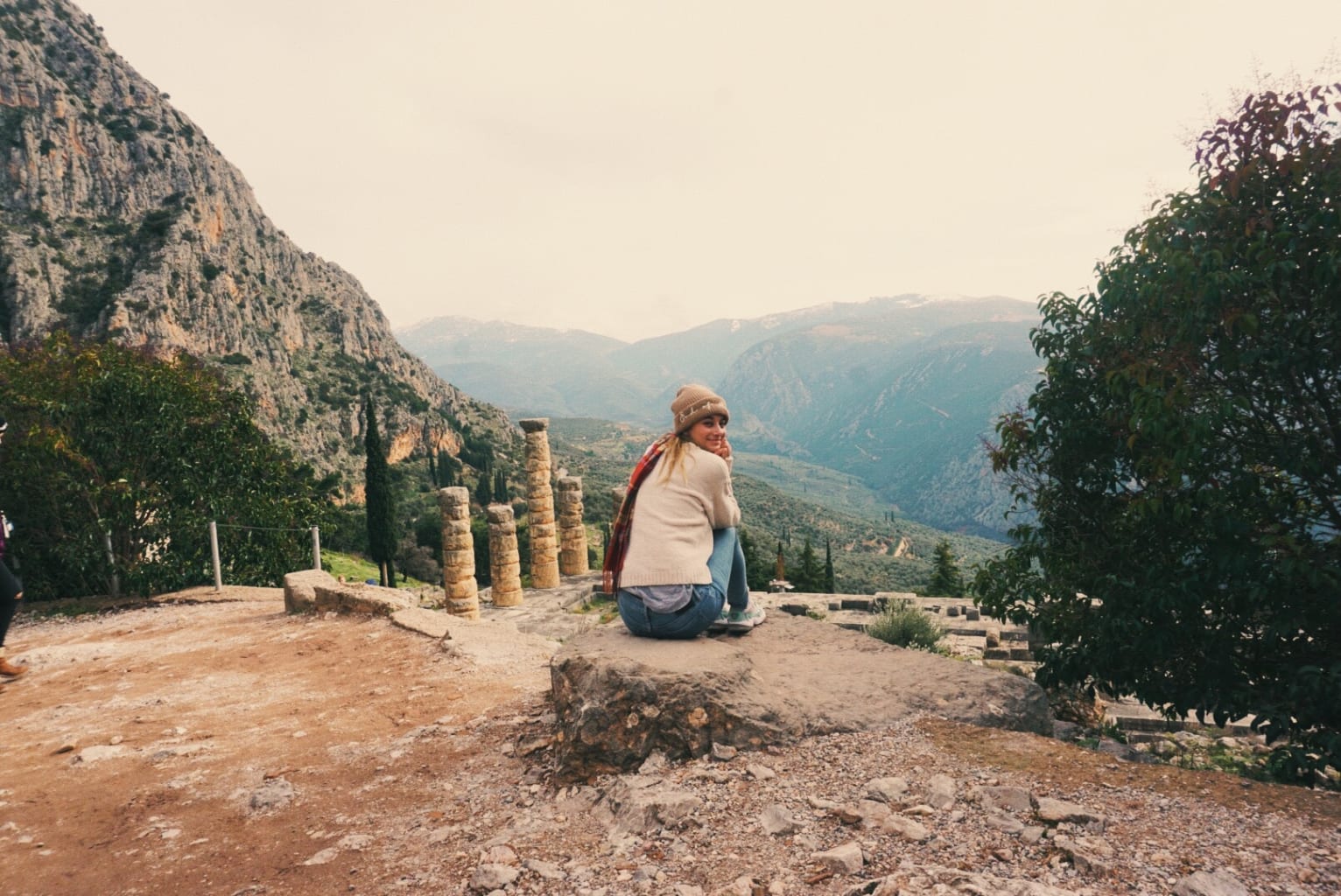 A student sitting on the ground, in front of a mountain view in Athens.