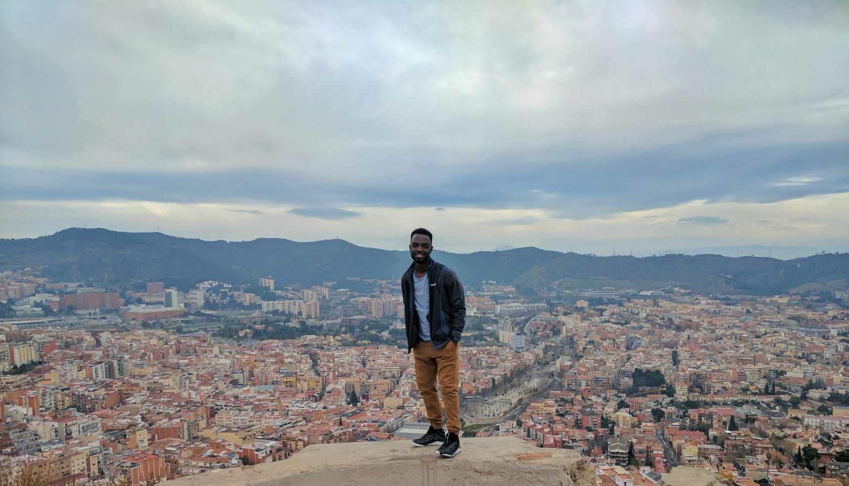 A student standing on a rock overlooking a view of the Barcelona cityscape.