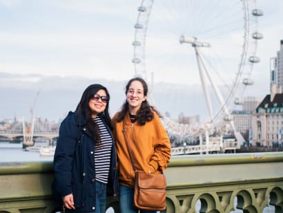 Two students in London, posing on a bridge with a ferris wheel in the background.