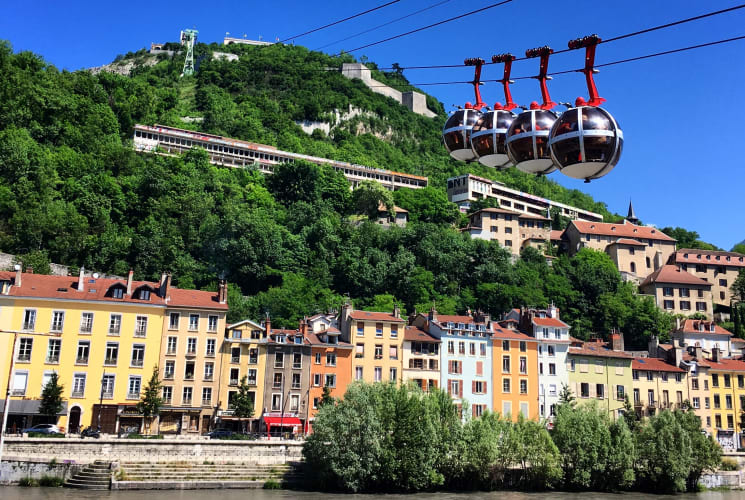 Four cable cars moving up, passing over buildings in Grenoble, France.