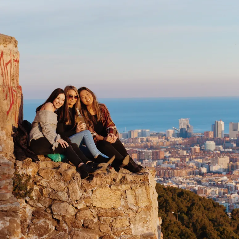 Three students sitting on a cliff overlooking a city in Spain.