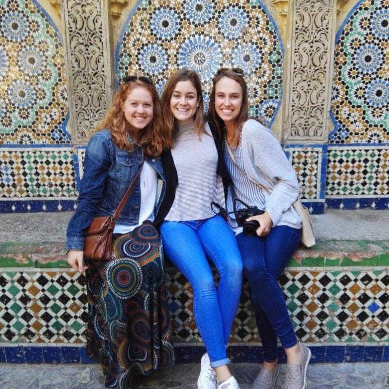 Three students sitting together near a decorative wall in Spain.